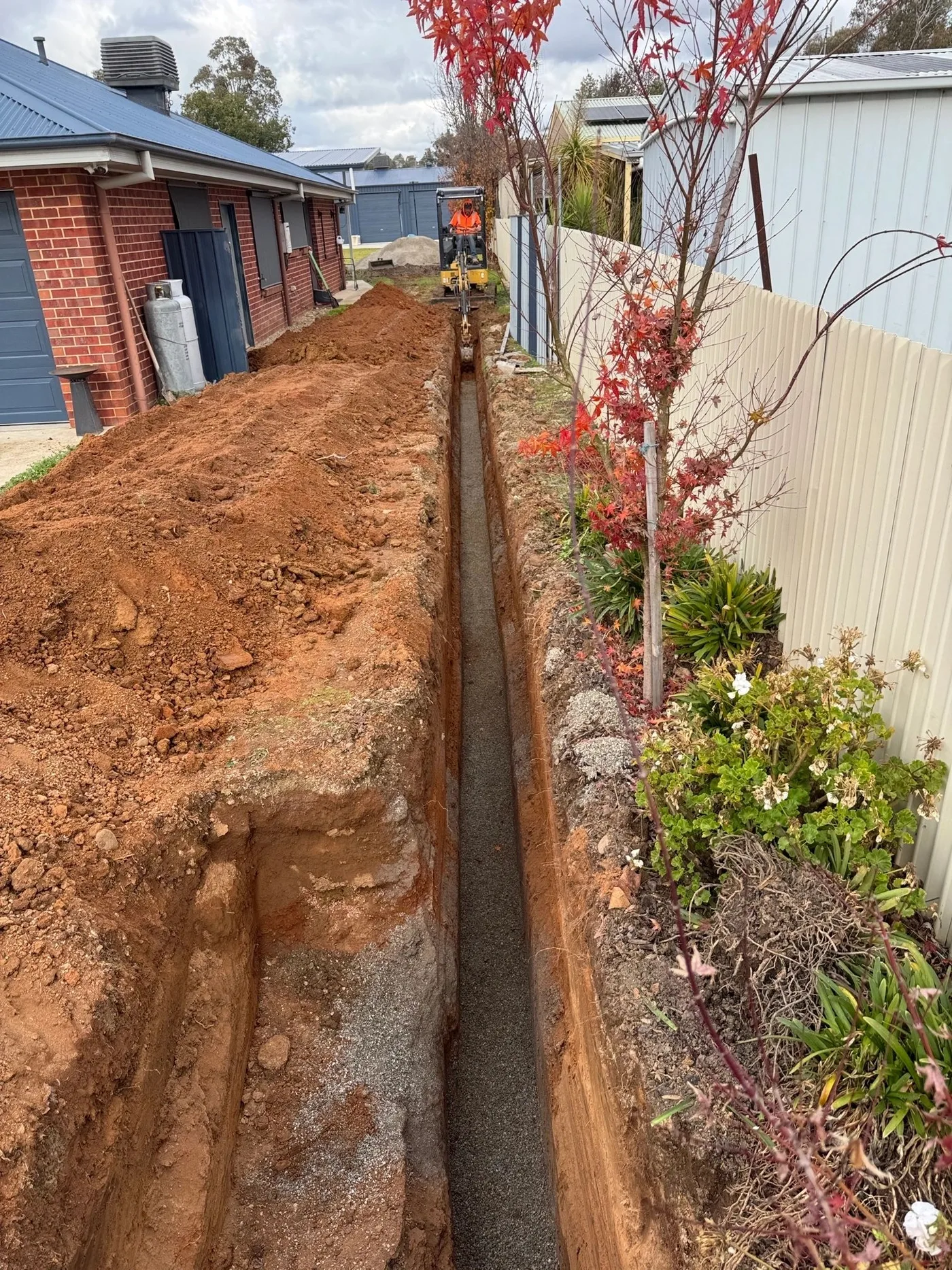 Licensed plumber digging a sewer line beside a home